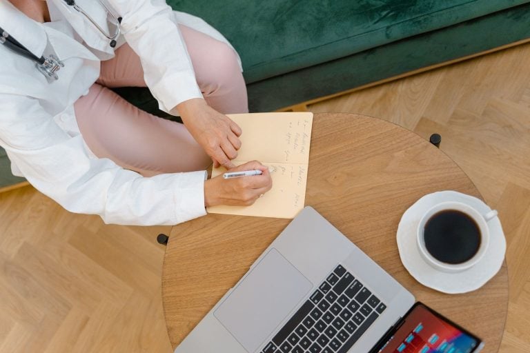 CPD credits: a doctor writing learning notes in a notebook beside a laptop
